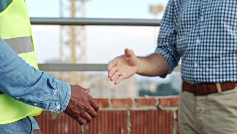 Close-up-of-the-African-American-and-Caucasian-male-hands-shaking-at-the-building-site.-Builder-greeting-with-foreman-or-architect.